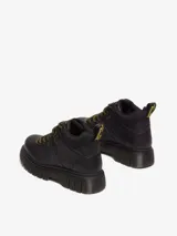 Botín de cuero negro Dr. Martens modelo Woodard, con cuello acolchado, cordones de tipo excursionista en amarillo y negro, suela acanalada Club Wedge con pespunte negro y tirador trasero con logo.