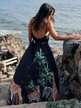 Vestido largo negro con estampado de jungla con palmeras, jirafas y leopardos. Tiene breteles finos, escote en V cruzado y cinturón con apliques brillantes.