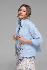 Campera corta color coral con cuello camisero, cierre frontal con botones, bolsillos de parche en el pecho y mangas largas con puños abotonados. Presenta calados tipo broderie en hombros, mangas y espalda.