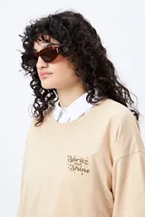 Remera blanca de corte holgado con mangas cortas y cuello redondo. Estampado pequeño en el frente con la frase "Spritz and Shine" en verde.