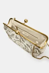 Bolso de mano tipo clutch color crema, con cierre metálico dorado y apliques florales bordados con lentejuelas y cuentas plateadas, doradas y negras.