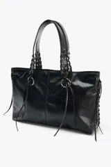 Bolso shopper de hombro color marrón, con flecos y trenzados en el cuerpo. Tiene doble cremallera metálica, asa doble con detalles metálicos y trenzados, y bolsillo interior. Cierre mediante cremallera metálica.