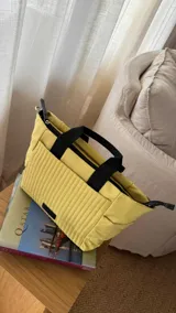 Cartera negra tipo tote bag con diseño capitoneado, doble asa corta y correa larga ajustable. Incluye bolsillos laterales y bolsillo frontal amplio.
