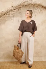 Blusa de lino color beige, con detalles de punto escama en escote y mangas, y prendedor de flor en el hombro. Talle único.