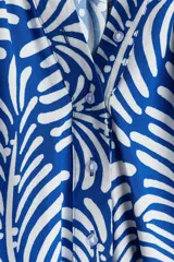Blusa con estampado de hojas en azul y blanco, de tejido liviano, con cuello corto fruncido y tapeta de botones. Mangas globo largas con volumen de corte raglán y puños finos abotonados.