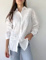 Camisa blanca de mangas largas con detalles de broderie en el frente, mangas y espalda. Corte recto, cuello clásico y cierre frontal con botones.