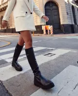 Bota de caña media de cuero negro, con suela track y cierre lateral.