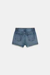 Shorts de jean de algodón, tiro alto, color azul claro desgastado. Presenta cinco bolsillos, cierre frontal con botón metálico y bajo desflecado con vuelta.
