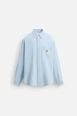 Camisa celeste de denim ligero de algodón, corte relaxed fit, con cuello abotonado, manga larga con puños abotonados, bolsillo de parche en el pecho con bordado y cierre frontal abotonado.
