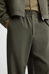 Pantalón largo color verde oscuro, de corte recto y tiro medio. Confeccionado en tejido con viscosa, con cintura elástica, bolsillos laterales y trasero de vivo. Cierre frontal con cremallera y botón.