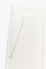 Pantalón de tiro alto color blanco, confeccionado en hilatura con viscosa, con bolsillos laterales y de plastrón en espalda. Detalle de costura marcada en delantero e hilo a contraste. Cierre frontal con cremallera, botón interior y gancho metálico.