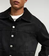 Campera masculina de jean negro con efecto desteñido, modelo boxy, con cuello solapa, manga larga con puño abotonado, cierre frontal con botones, bolsillos grandes y recortes.
