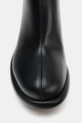 Botín negro de cuero sintético con cuña alta y punta redonda. Cierre con cremallera lateral.