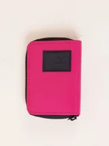 Billetera fucsia con cierre de cremallera y parche de goma negro con logo.