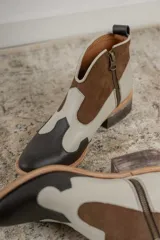 Botines de cuero marrón y blanco con diseño western, puntera redondeada y cierre lateral con cremallera. El talón tiene una tira de cuero para facilitar el calce.