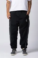 Pantalón de jogging negro de taslan con corte holgado, cintura elástica con cordón ajustable, bolsillos laterales y puños elásticos. Presenta una franja blanca a lo largo de la pierna y logo bordado en blanco.