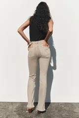 Pantalón de jean color beige, de tiro alto, corte ajustado en la cadera y muslos, y acampanado desde la rodilla. Tiene cinco bolsillos y cierre frontal con cremallera y botón.