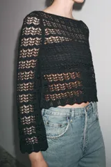 Jersey corto de punto calado negro, con cuello redondo amplio y mangas largas acampanadas.