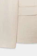 Blazer color beige de cuello solapa y manga larga. Tiene bolsillos con solapa en el delantero y cierre frontal con un botón.