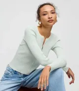 Cardigan de punto acanalado color verde menta y blanco, de manga larga y corte ajustado. Presenta un escote redondo con cierre frontal de cremallera doble.