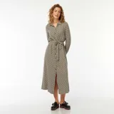 Vestido camisero largo con estampado geométrico en tonos beige, negro y blanco. Tiene cuello camisero, mangas largas con puños abotonados, cierre frontal con botones y cinturón de lazo.