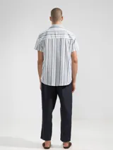 Camisa de manga corta a rayas verticales azules y blancas, con cuello clásico, corte cuadrado y calce relajado. Presenta botones de coco con logo y parche distintivo de Polonio. Confeccionada en Italia con mezcla de lino y algodón.