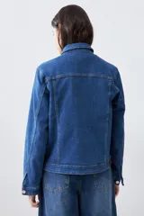 Campera clásica de jean color azul medio, con cuello clásico, cierre frontal con botones, bolsillos con solapa en el pecho y mangas largas con puños abotonados.