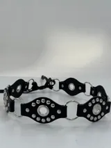Cinto negro de cuero sintético con apliques de tachas plateadas y argollas metálicas.