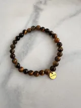 Pulsera elástica de piedras naturales color marrón con dije circular dorado con la palabra "AIRE" grabada.
