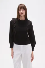 Blusa de algodón color negro con cuello a la base y detalle de volados en el frente. Posee mangas largas con puños elásticos y un panel frontal con textura fruncida.