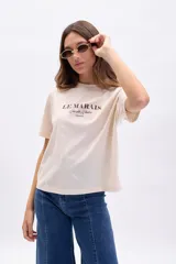 Remera color crudo de manga corta con cuello redondo y estampa marrón con la frase "Le Marais, Rue des Rosiers, France".