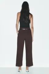 Pantalón marrón de tiro alto con cinturón negro, bolsillos delanteros y cierre frontal con cremallera y gancho metálico.