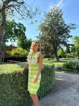 Vestido tejido en hilo de algodón, a rayas verticales verdes y blancas, con volados en los hombros y cierre frontal con botones.