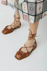 Sandalias bajas color marrón con tiras de cuero entrecruzadas y cordones para atar al tobillo.