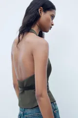 Top de cuello halter color verde oscuro, con escote pico, falso bolsillos de vivo en delantero y cinturón negro con hebilla metálica. Cierre frontal con cremallera oculta.