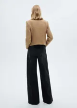 Chaqueta corta color beige de tweed con cuello mao, cierre frontal con botones y cuatro bolsillos delanteros con solapa.
