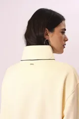 Buzo color crema con cuello alto con botones y ribete negro en cuello, puños y ruedo.