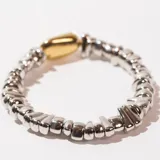 Pulsera elástica con cuentas irregulares plateadas y una cuenta central ovalada dorada.