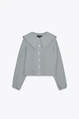 Camisa de manga larga con puños elásticos y cuello bobo con volantes. Cierre frontal con botones.