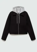 Chaqueta negra corta con capucha gris desmontable y ajustable con cordones. Presenta cuello camisero, cierre de cremallera doble, bolsillos laterales y bajo con goma elástica.