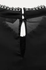 Blusa negra de viscosa con cuello perkins y manga larga. Detalles de bordados, lentejuelas y volantes. Cierre en la espalda con abertura y botones.