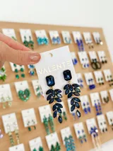 Par de aros colgantes con base de forma rectangular y diseño de hojas colgantes, con incrustaciones de strass color azul. Cierre de gancho.