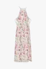 Vestido largo con estampado floral, cuello redondo y tirantes finos. Presenta elástico en la cintura con aberturas y lazadas laterales, volantes en el mismo tejido, forro interior a contraste y abertura frontal en el bajo. Cierre en la espalda con botón.