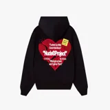 Campera negra con capucha, corte oversize y estampado de corazón roto con texto en la espalda. Incluye un sticker amarillo con texto manuscrito.