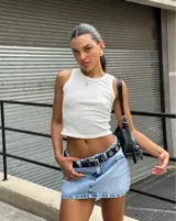 Minifalda de jean celeste con lavado claro, corte ajustado y cinturón de cuero negro con hebilla plateada y ojales metálicos.