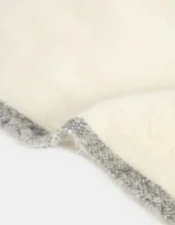 Bufanda tejida color crema con flecos en los extremos y etiqueta de cuero sintético negra.
