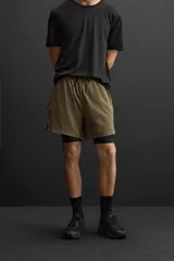 Shorts deportivos color verde oliva con calza interior negra, de tejido técnico ligero y elástico. Cuenta con cintura elástica ajustable con cordón, bolsillos laterales con cierre de cremallera, bajo con aberturas laterales y detalle de logo estampado.