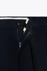 Pantalón de vestir azul marino de lana, con tiro bajo, cintura con trabillas, bolsillos laterales, raya planchada y cierre frontal con cremallera, botón y gancho metálico.