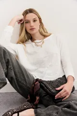 Remera blanca de algodón con calce relajado y cuello redondo. Tiene mangas largas que se ajustan hacia los puños.