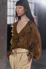 Blusa color marrón con escote en pico, manga larga abullonada con elástico en los puños y volantes en el escote y mangas.